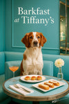 Brittany Spaniel on a turquoise banquette by a round table with tomato-topped tarts, cheese crostini, a peach-hued cocktail and white flower under “Barkfast at Tiffany’s” sign