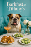 English Bulldog seated on a turquoise banquette beside a marble table with ham croissant sandwiches, cucumber rounds, a peach cocktail, mirrored gift box and white peonies under “Barkfast at Tiffany’s” script