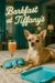 Chihuahua on a bed next to a peach cocktail glass, turquoise sleeping mask, pearl necklace and tray beneath Barkfast at Tiffany’s lettering