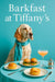 English setter wearing turquoise scarf seated at turquoise table with a plain brioche bun, two arugula sliders, a cream puff, peach cocktail and silver sugar bowl