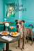 Pit Bull standing beside a teal banquette at a round riveted café table with two muffins tomato topped toasts a pink cocktail and a white flower