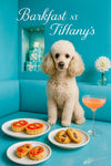 Cream poodle seated on a teal banquette beside plates of tomato tartlets, mini tomato bites, chocolate-chip cookies and a pink cocktail