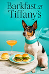 Rat Terrier wearing a turquoise scarf seated at a marble café table with two mini arugula sliders a brioche bun top a peach cocktail and a fork by a turquoise banquette