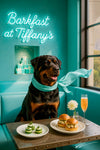 Rottweiler wearing a turquoise scarf seated on a tufted teal banquette under a glowing neon Barkfast sign in a chic café setting