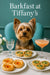 Yorkshire terrier seated on a teal chair behind a white table with plates of apricot jam tarts spinach quiches a peach cocktail a water glass and white lisianthus