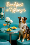 Australian Shepherd wearing a Tiffany-blue scarf seated at a turquoise café table with mini spinach quiches, cheese tartlets, a peach cocktail, and a white dahlia under a neon Barkfast sign