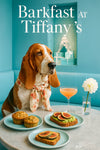 Basset Hound wearing a floral scarf seated at a Tiffany-blue café table with two bran muffins, avocado toast topped with figs, fig-topped ricotta toast, a peach cocktail, and a white dahlia