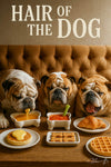 Three bulldogs at a table with pancakes, waffles, croissant, dog biscuits, and drinks under a “Hair of the Dog” sign