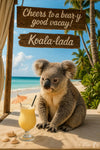 Koala sitting on the beach with a tropical cocktail under a wooden sign that says Cheers to a bear-y good vacay in artwork titled Koala-lada