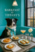 Border Collie wearing a teal scarf seated in a turquoise booth next to a table with a peach Danish, ricotta-topped toasts, water glasses, a peach cocktail, and a white dahlia bloom