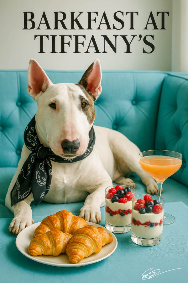 White Bull Terrier wearing a black paisley bandana perched on a tufted turquoise banquette with its paws on a table holding three croissants, two berry parfaits in jars and a blush-hued cocktail under “Barkfast at Tiffany’s” script