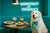 Great Pyrenees dog wearing teal bow enjoying brunch in teal café setting on metal print