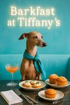 Italian Greyhound wearing a teal scarf seated at a dark wood table with whipped cheese crostini sugar muffins and a pink cocktail
