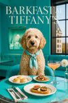 Cream Labradoodle wearing a teal silk scarf seated on a turquoise banquette with scones, fig toasts, and a peach cocktail on a glossy table