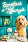 Cream-colored labradoodle seated at marble café table with cucumber finger sandwiches berry parfait mimosa and white dahlia beneath neon Barkfast at Tiffanys sign