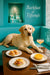 Golden Labrador Retriever lounging on turquoise banquette at wooden café table with ham croissants orange tart and peach cocktail under Barkfast at Tiffanys sign and turquoise gift boxes