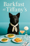 Curly black Mudi wearing an ivory scarf seated at a turquoise café table with two spinach quiches apple-topped toast a peach cocktail and a white dahlia under Barkfast at Tiffany’s sign