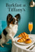 Tricolored Papillon perched on a teal chair beside a white-clothed table with two croissants jam pastry and a flute of mimosa under a gold pendant lamp