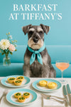 Whiskered Schnauzer wearing a turquoise scarf seated on a teal café banquette beside a vase of pastel flowers