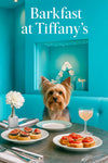 Silky Terrier seated at a turquoise banquette behind a metal table with fig-topped tartlets tomato tartines a peach brunch cocktail a white flower and Tiffany blue gift display