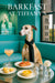 Whippet wearing a black scarf seated at a teal booth with lemon tartlets a lemon tart tomato toast a peach cocktail a glass of water and a white carnation in a vase