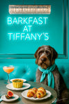 Wirehaired pointing griffon wearing a teal scarf seated under a neon Barkfast at Tiffanys sign with two salted croissants halved figs a green tart and a peach cocktail on a round metal table