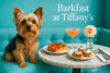 Yorkshire terrier sitting on a turquoise banquette looking at a marble table with a cherry tomato tart three ricotta crostini a peach cocktail and a white flower in a bud vase